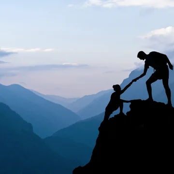 One hiker helping another up to a mountaintop